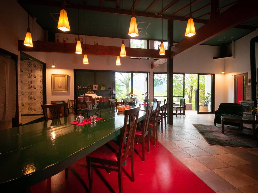 Uma sala de jantar ampla, com uma longa mesa verde, várias cadeiras e luminárias pendentes.