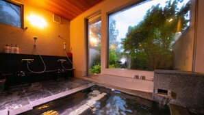 A spa area with a hot tub, a window with a view of greenery, and a wall-mounted heater.