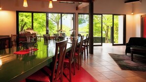 Un comedor amplio con una mesa larga, sillas y vistas a exuberante vegetación a través de amplios ventanales.