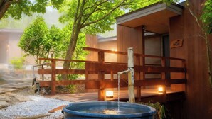 A traditional Japanese onsen with a wooden bathhouse, a stone pathway, and a wooden fence.