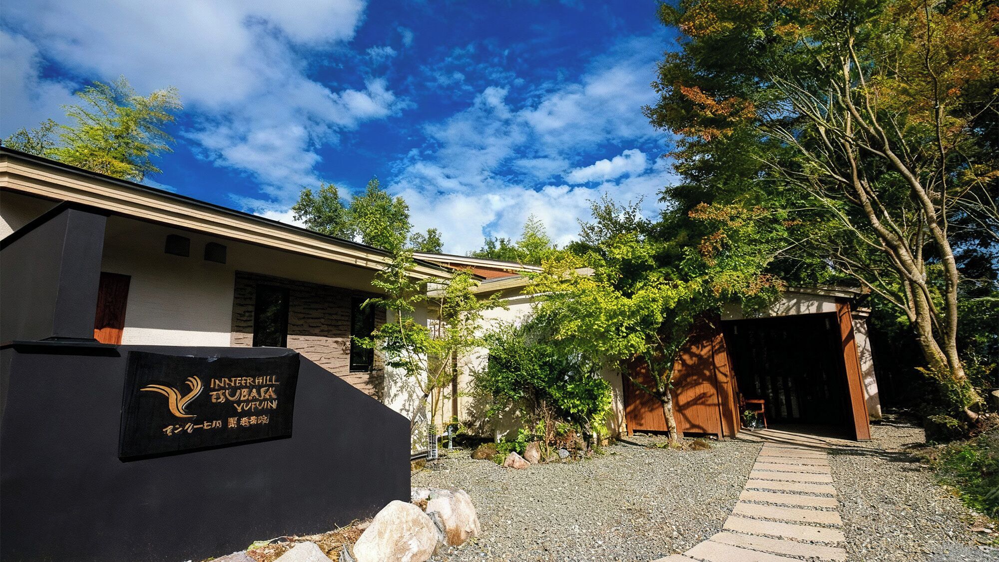 A building with a stone facade, a gravel pathway leading to a wooden door, and a sign with text.