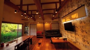 A spacious living area with a wooden dining table, a leather sofa, and a TV mounted on the wall.
