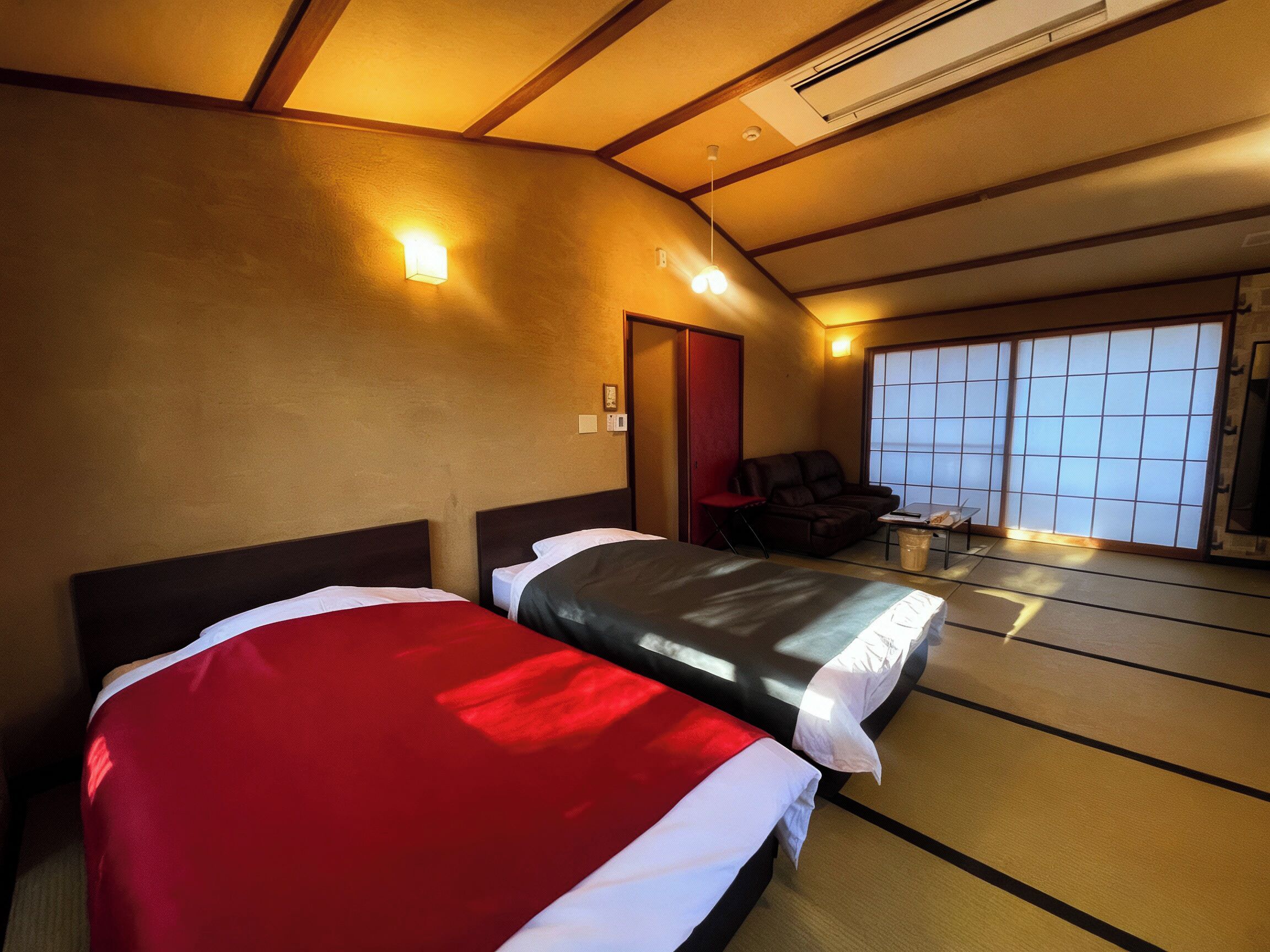 A hotel room with two beds, a sofa, a chair, a small table, and a sliding door leading to a balcony.