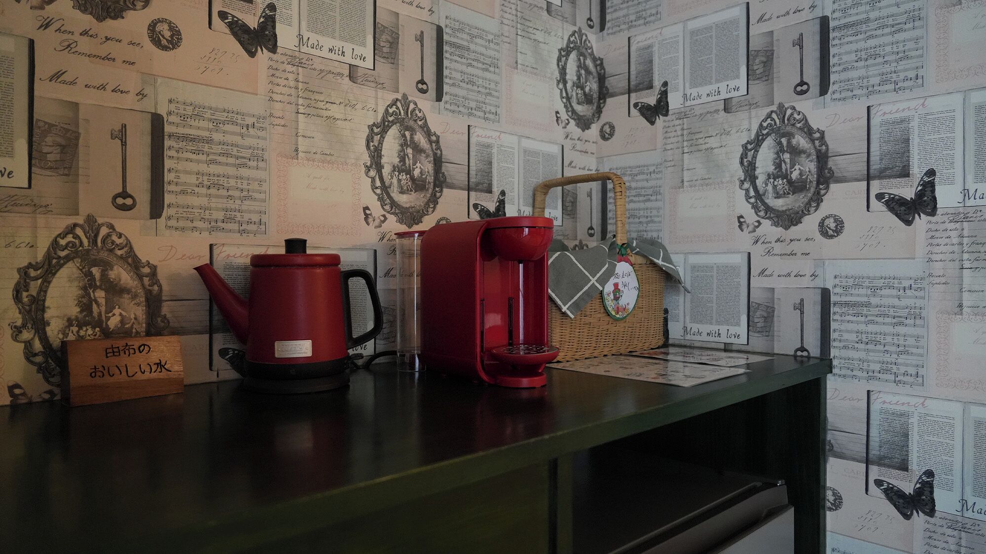 Uma bancada de cozinha com uma chaleira vermelha, uma cafeteira vermelha e uma cesta de vime com uma etiqueta.