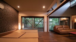 A modern interior with tatami mats, a leather sofa, and large windows offering a view of trees.