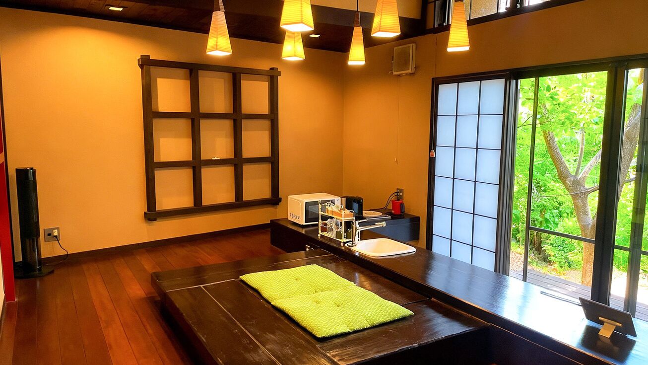 Una habitación con piso de madera, una toalla verde, un lavamanos, una ventana con vistas a la vegetación y una puerta corredera japonesa tradicional.