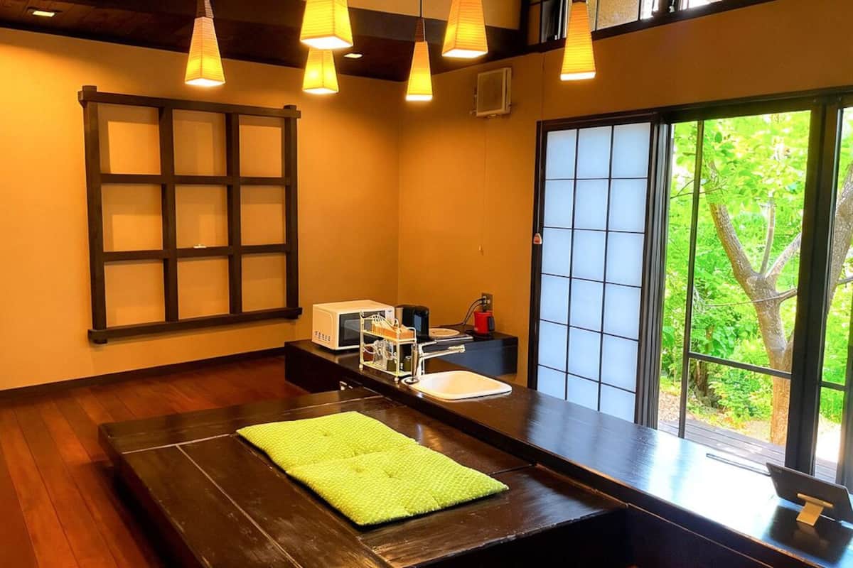 Um quarto com piso de madeira, toalha verde, pia, janela com vista para vegetação e uma porta tradicional japonesa deslizante.