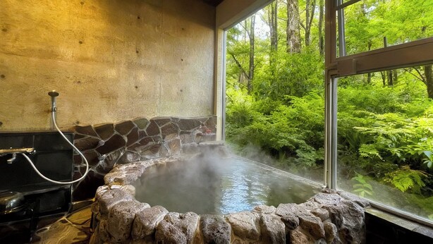 A stone hot tub with a steam shower, surrounded by a stone wall and a window overlooking a forest.