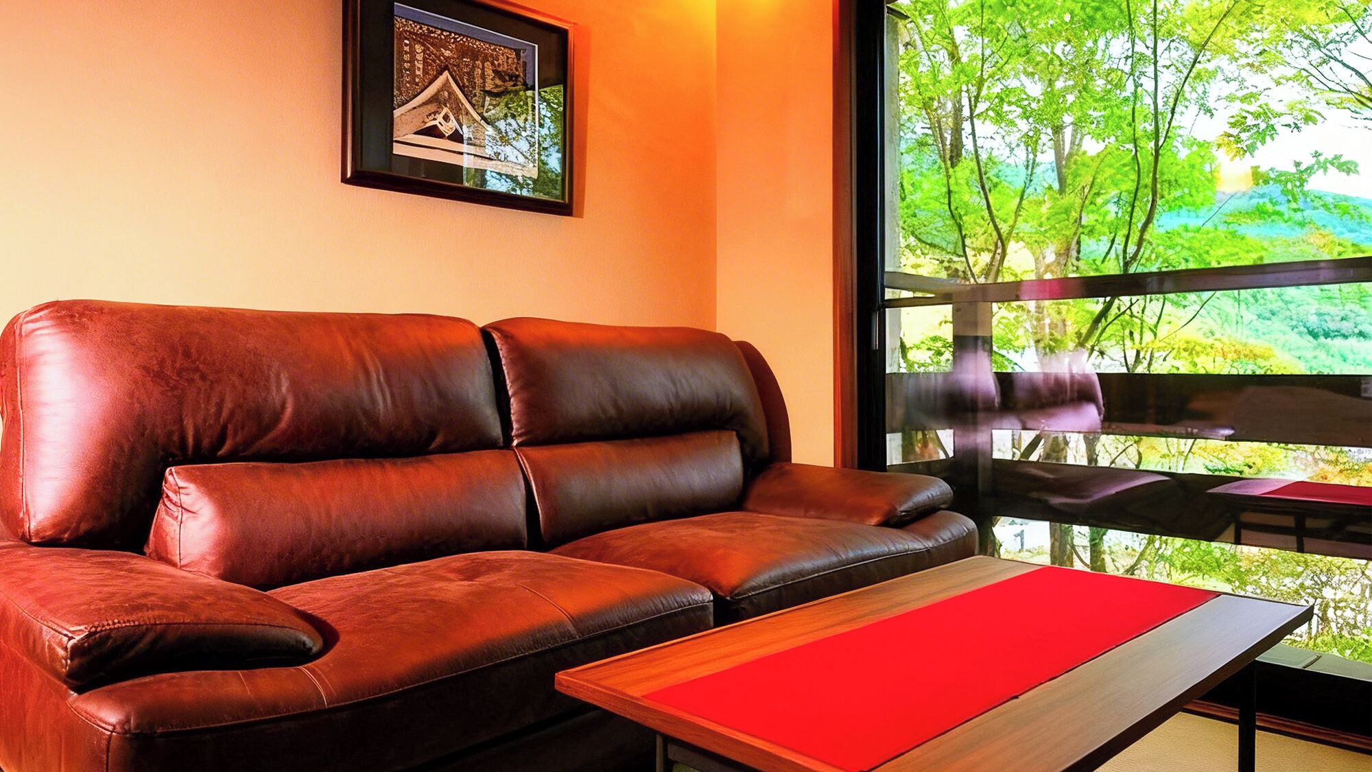 Un sofá de cuero marrón con un cojín rojo, una mesa de centro de madera y un cuadro en la pared.