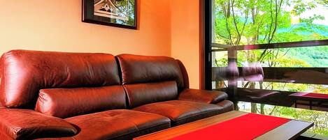 Un sofá de cuero marrón con un cojín rojo, una mesa de centro de madera y un cuadro en la pared.