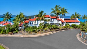 A coastal resort with white buildings and red roofs, surrounded by palm trees and a clear blue sky. - Bella Vista East 3 Luxury Ocean Views Large Flat Grassed Area + Buggy (Whitsundays)