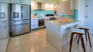 A modern kitchen with stainless steel appliances, a central island, and bar stools. - Bella Vista East 3 Luxury Ocean Views Large Flat Grassed Area + Buggy (Whitsundays)