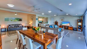 A spacious living area with a wooden dining table, white chairs, a sofa, and a TV. - Bella Vista East 3 Luxury Ocean Views Large Flat Grassed Area + Buggy (Whitsundays)