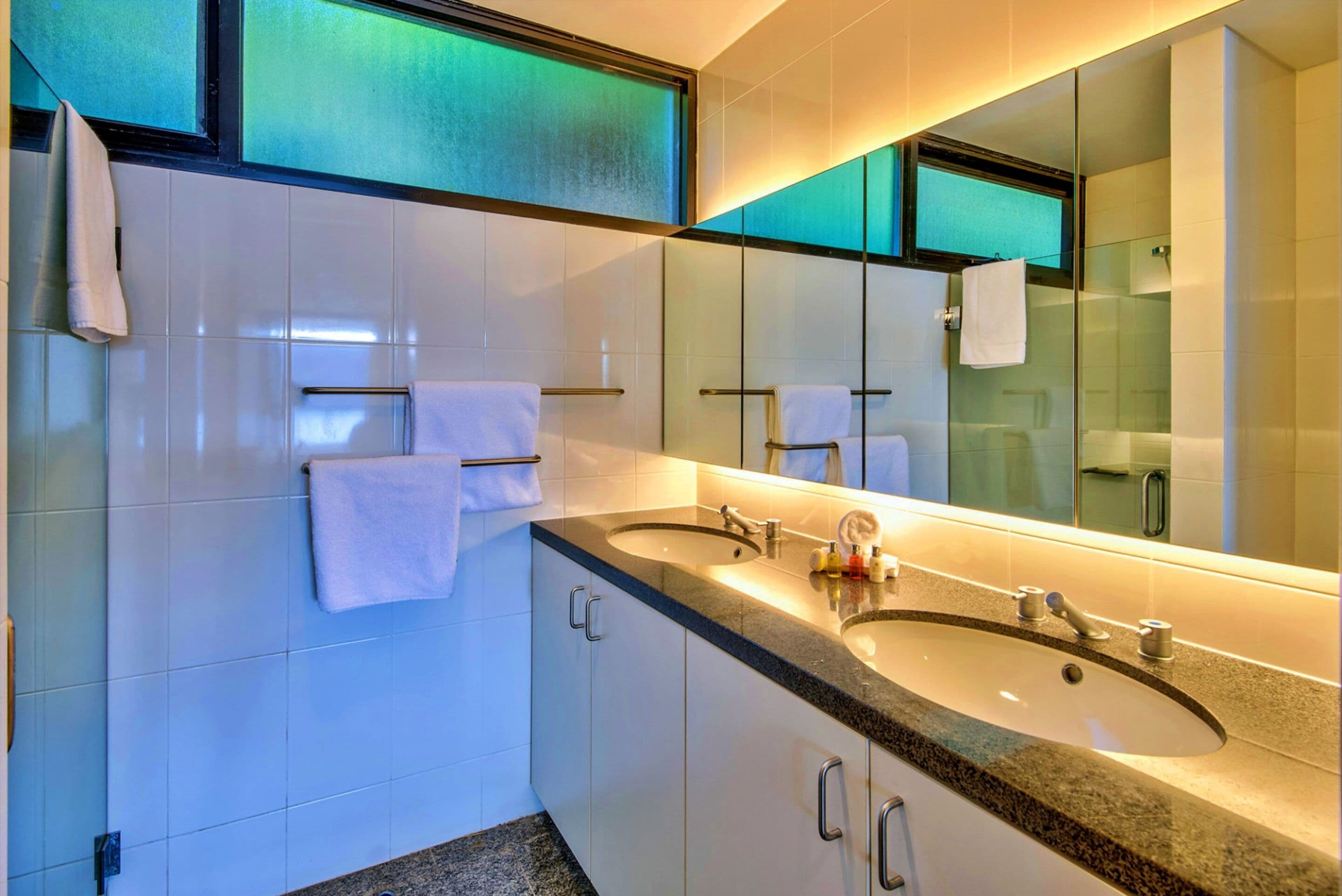 A modern bathroom with two sinks, a large mirror, and a glass shower enclosure.