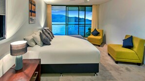 A modern hotel room with a large bed, a yellow armchair, and a view of a lake. - Waves 5 Luxury 3 Bedroom (Whitsundays)