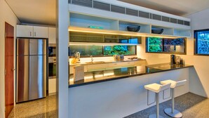 A modern kitchen with a stainless steel refrigerator, a built-in oven, a sink, and a bar area with stools. - Waves 5 Luxury 3 Bedroom (Whitsundays)