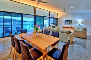 Een moderne woonkamer met een grote houten eettafel, comfortabele zitmogelijkheden, een bank en uitzicht op zee.