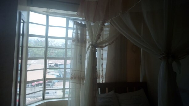 A room with a bed, a window with curtains, and a view of the outside. - 3 Shades Annex - Adults Only (Thika)