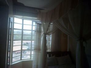 A room with a bed, a window with curtains, and a view of the outside. - 3 Shades Annex - Adults Only (Thika)