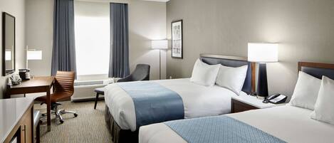 A hotel room with two beds, a desk, a chair, a desk lamp, a phone, and a window with curtains.