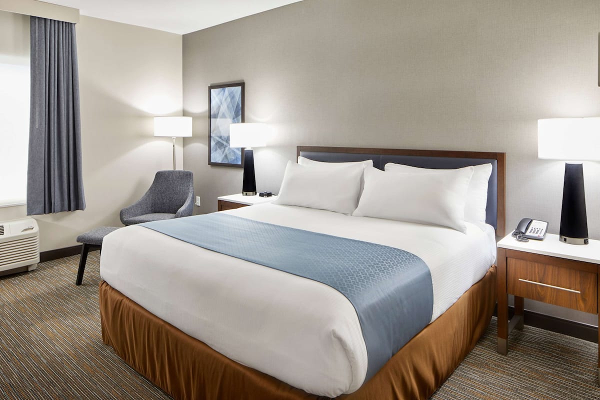 A hotel room with a large bed, two bedside tables, a chair, a desk, a lamp, and a painting on the wall.