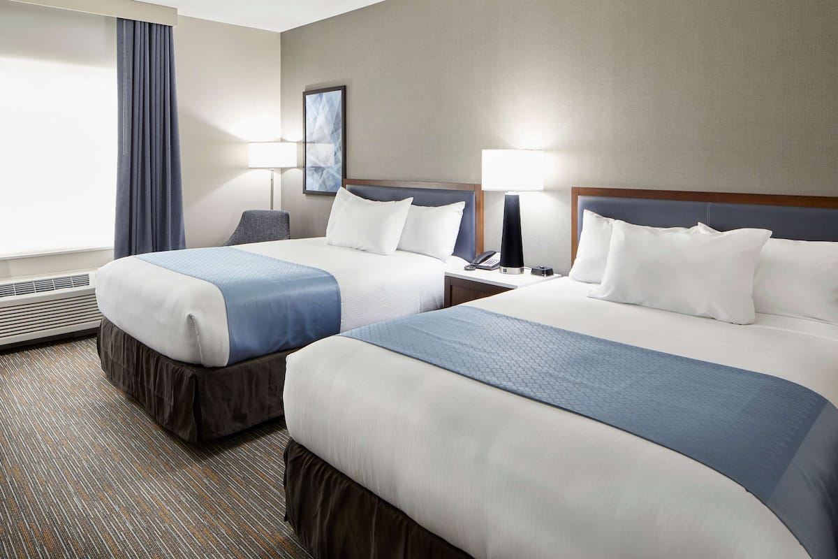 A hotel room with two beds, a desk, a chair, a lamp, and a window with curtains.