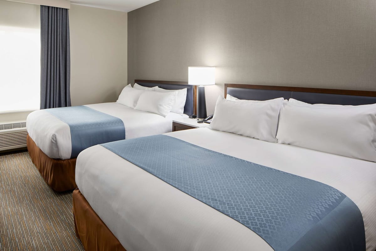 A hotel room with two beds, a nightstand with a lamp, and a window with curtains.