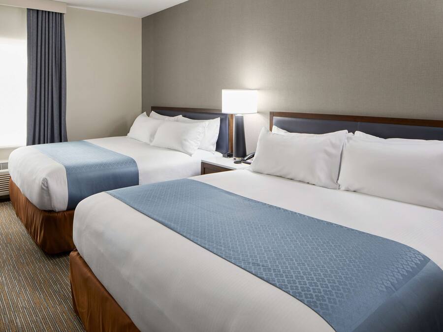 A hotel room with two beds, a nightstand with a lamp, and a window with curtains.