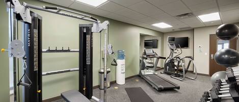 A gym with various exercise equipment, including a squat rack, treadmills, and dumbbells.