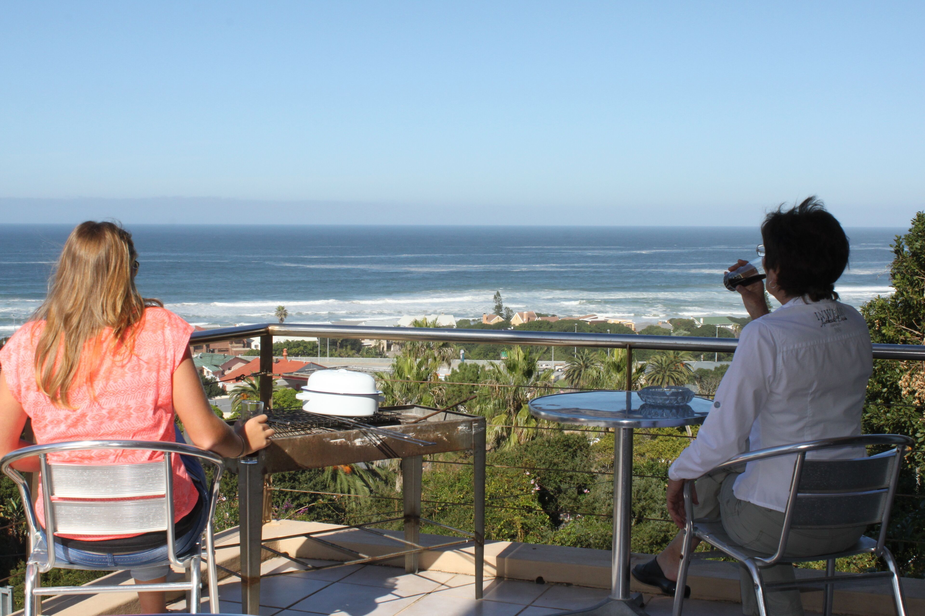Two people at a table with a grill, overlooking a coastal view.