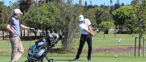 A golf course with a cart and a golfer in motion.