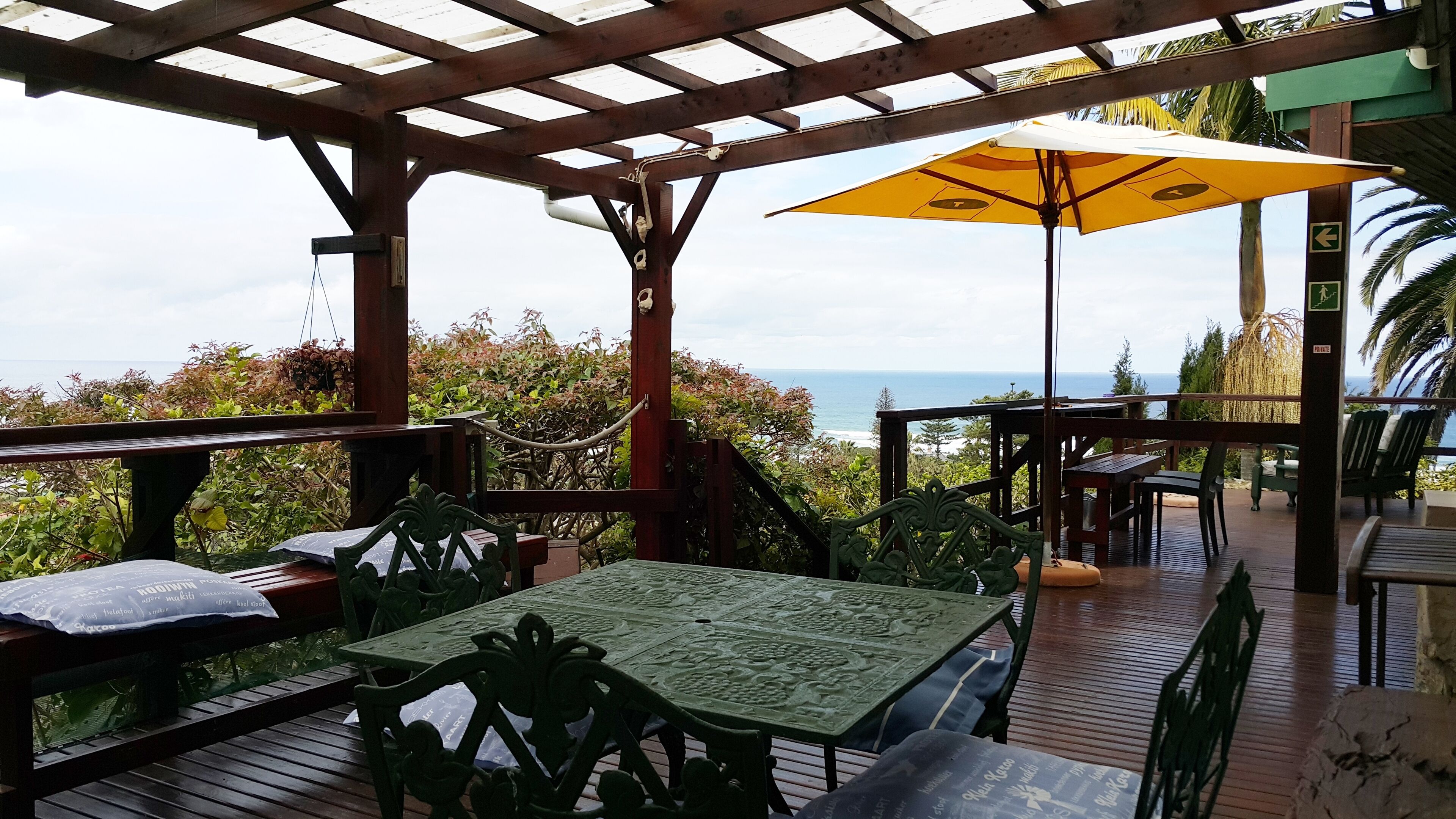 A covered outdoor seating area with tables and chairs, overlooking the ocean.