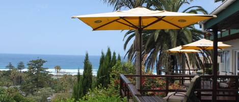 A wooden deck with outdoor seating and yellow umbrellas overlooking the ocean.
