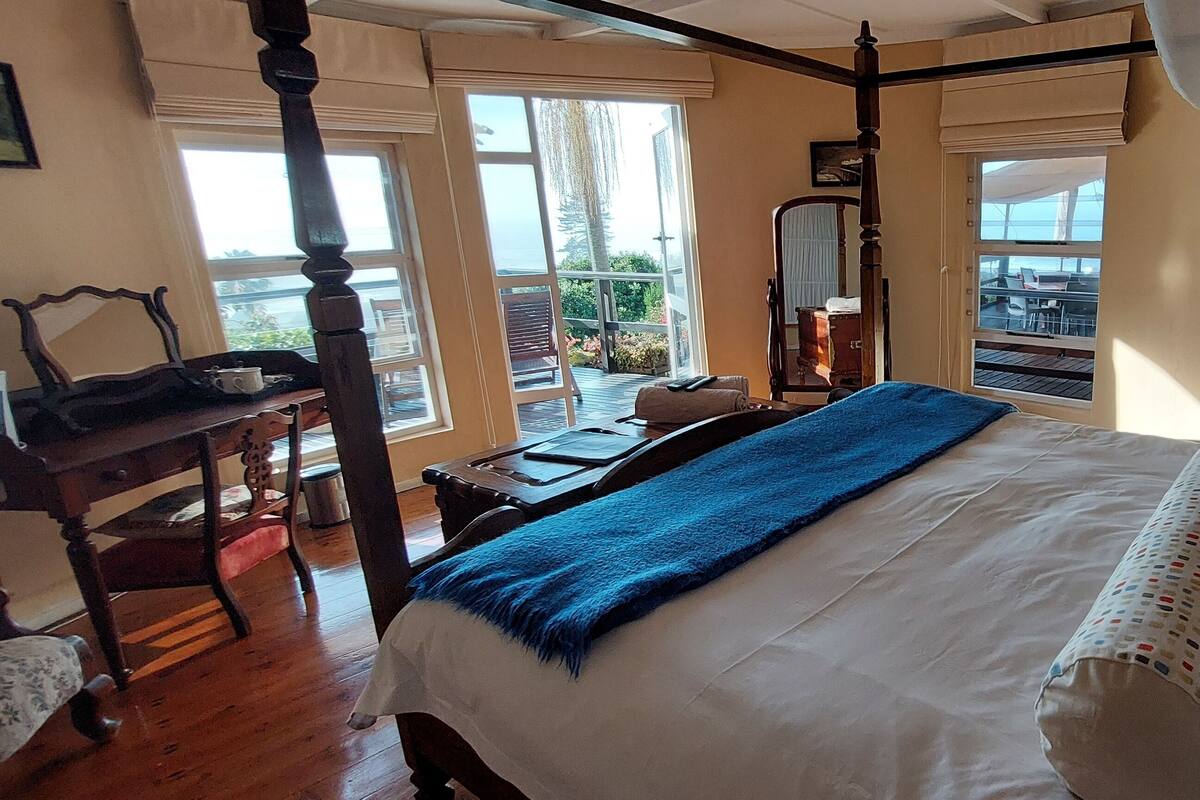 A bedroom with a large bed, a wooden chair, a desk, and a balcony with outdoor furniture.
