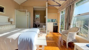 A bedroom with a bed, a shower, a sink, and a balcony with a chair. - The Tops (Wilderness)