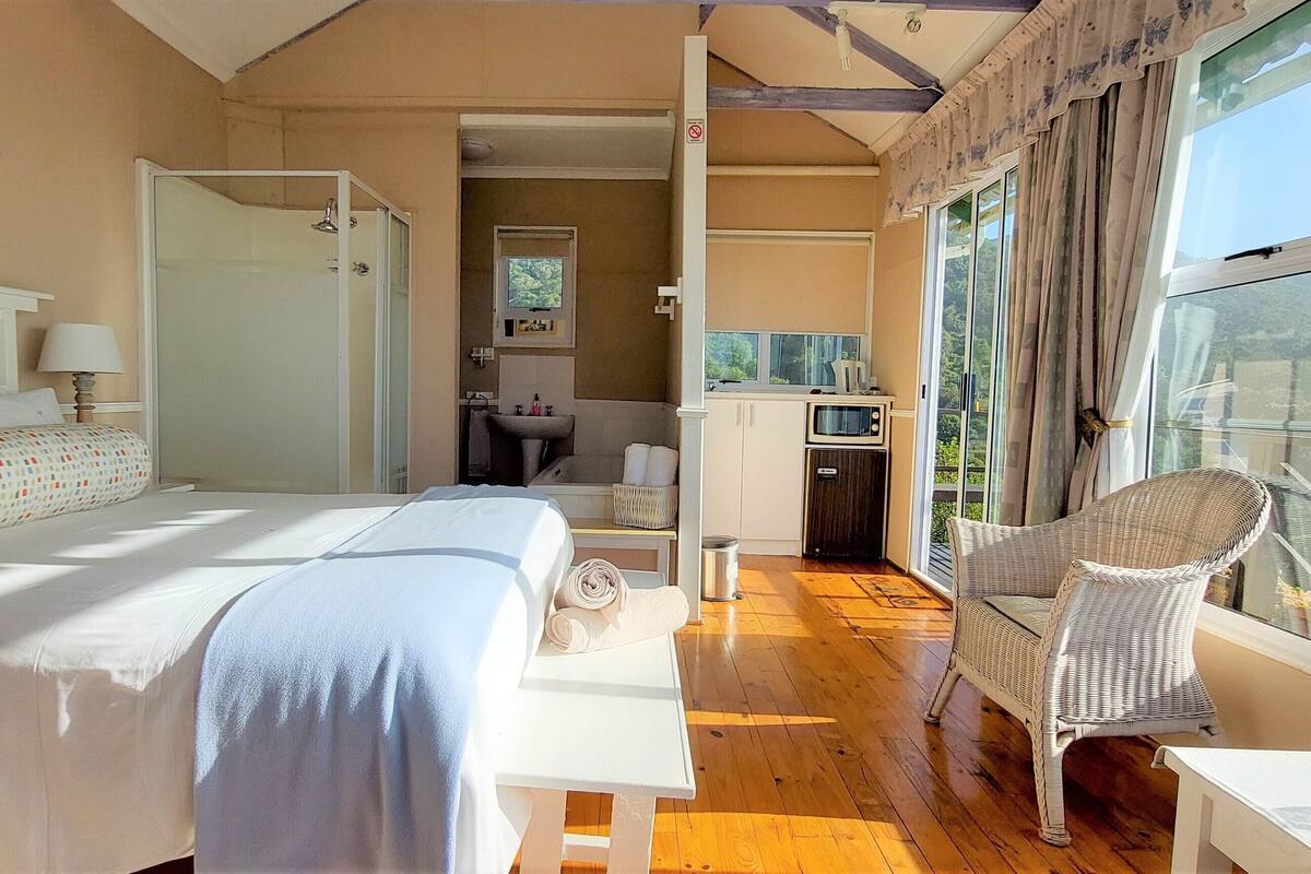 A bedroom with a bed, a shower, a sink, and a balcony with a chair.
