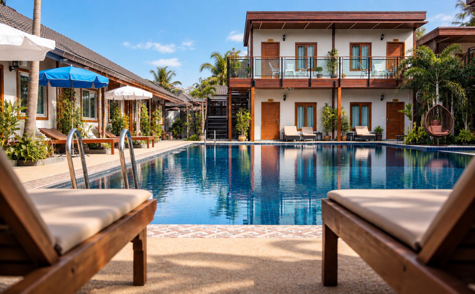A pool area with lounge chairs, a building with balconies, and palm trees.