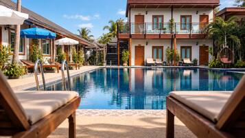 A pool area with lounge chairs, a building with balconies, and palm trees.
