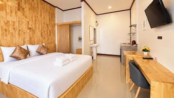 Habitación de hotel moderna con cabecera de madera, cama con ropa de cama blanca, escritorio con silla, televisor de pantalla plana montado en la pared y un baño pequeño con lavamanos y espejo.
