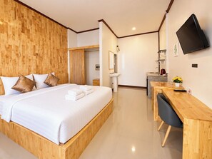Ein modernes Hotelzimmer mit Holz Kopfteil, einem Bett mit weißer Bettwäsche, einem Schreibtisch mit Stuhl, einem flachbildfernseher an der Wand und einem kleinen Badezimmer mit Waschbecken und Spiegel.