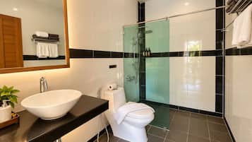 Un baño moderno con un lavamanos grande blanco, un inodoro y una zona de ducha con mampara de vidrio.