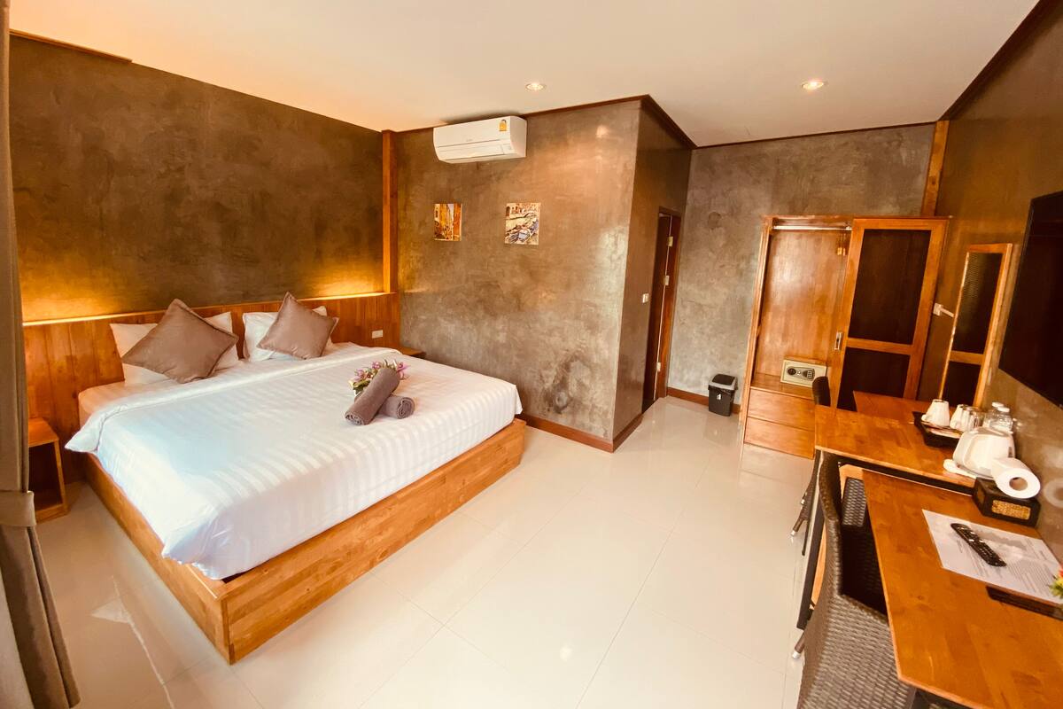 A modern hotel room with a large bed, wooden headboard, and a small desk with a chair.