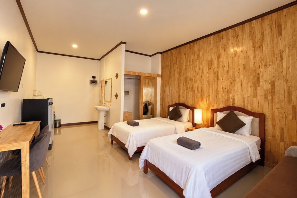 A hotel room with two beds, a desk, a TV, and a bathroom.