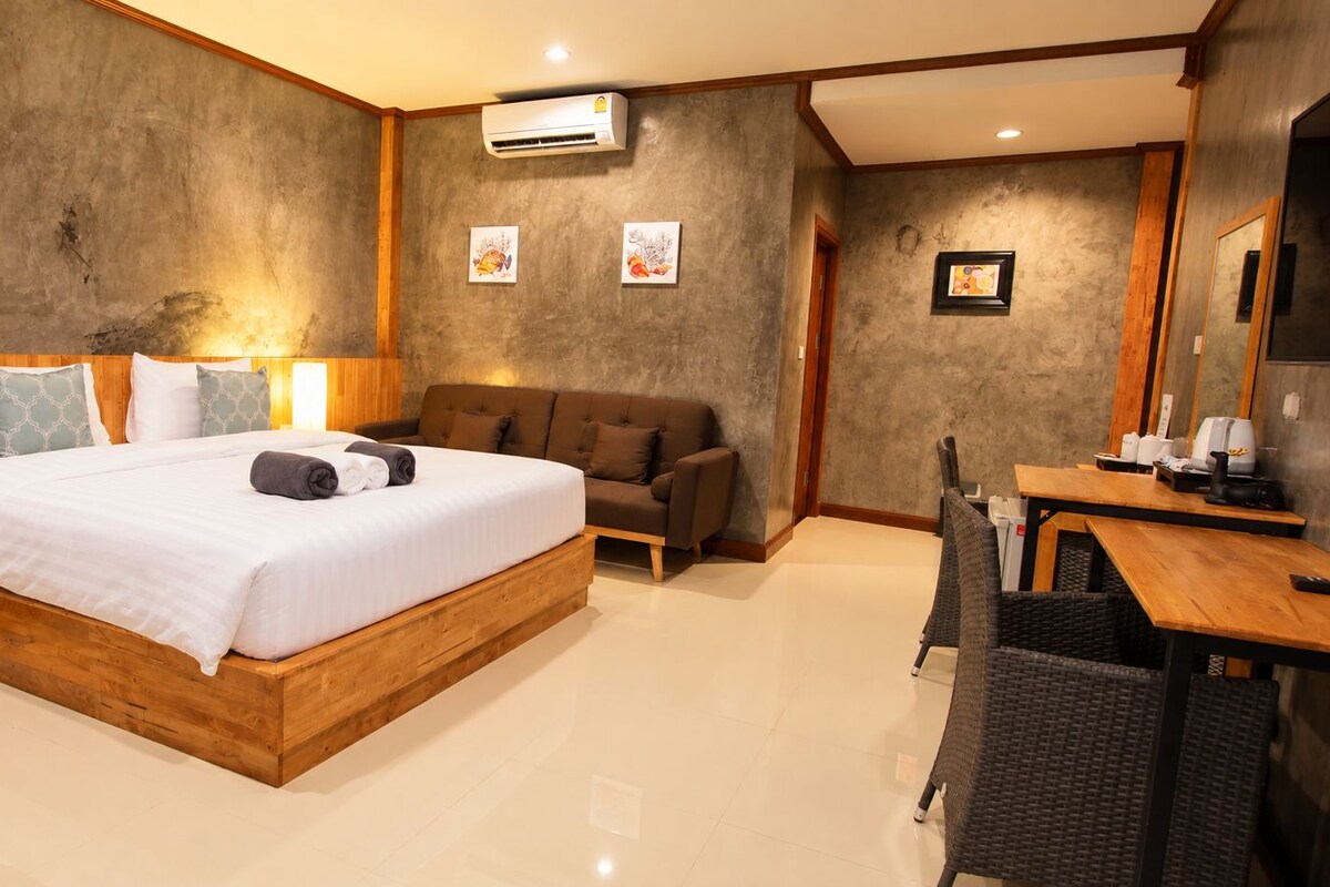A modern hotel room with a wooden bed, a sofa, a dining table, and a chair.