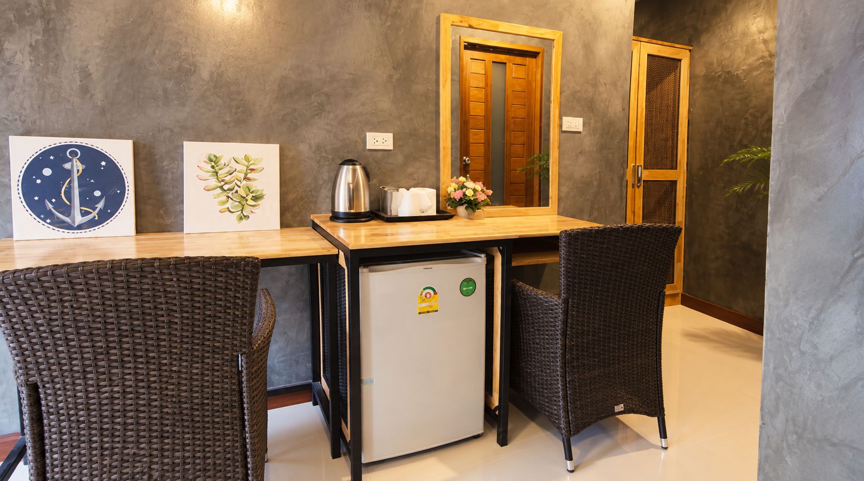 Una kitchenette equipada con refrigerador, cafetera y tostadora. Se observan dos sillas de mimbre y una mesa de madera.