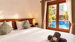 A hotel room with a bed, pillows, a nightstand, a lamp, and a view of an outdoor swimming pool. - Paradise Land Resort (Pattaya)