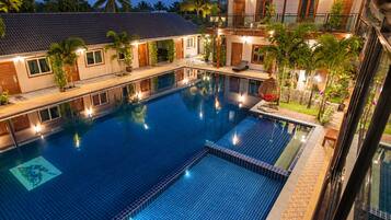 A large indoor swimming pool with a tiled floor, surrounded by a building with multiple balconies and windows.