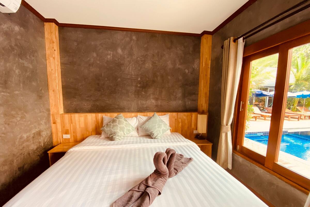 A hotel room with a large bed, wooden headboard, and a view of a swimming pool.