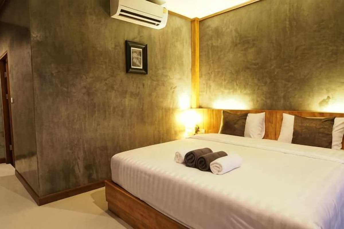 A hotel room with a bed, bedside lamps, a framed picture, and an air conditioning unit.