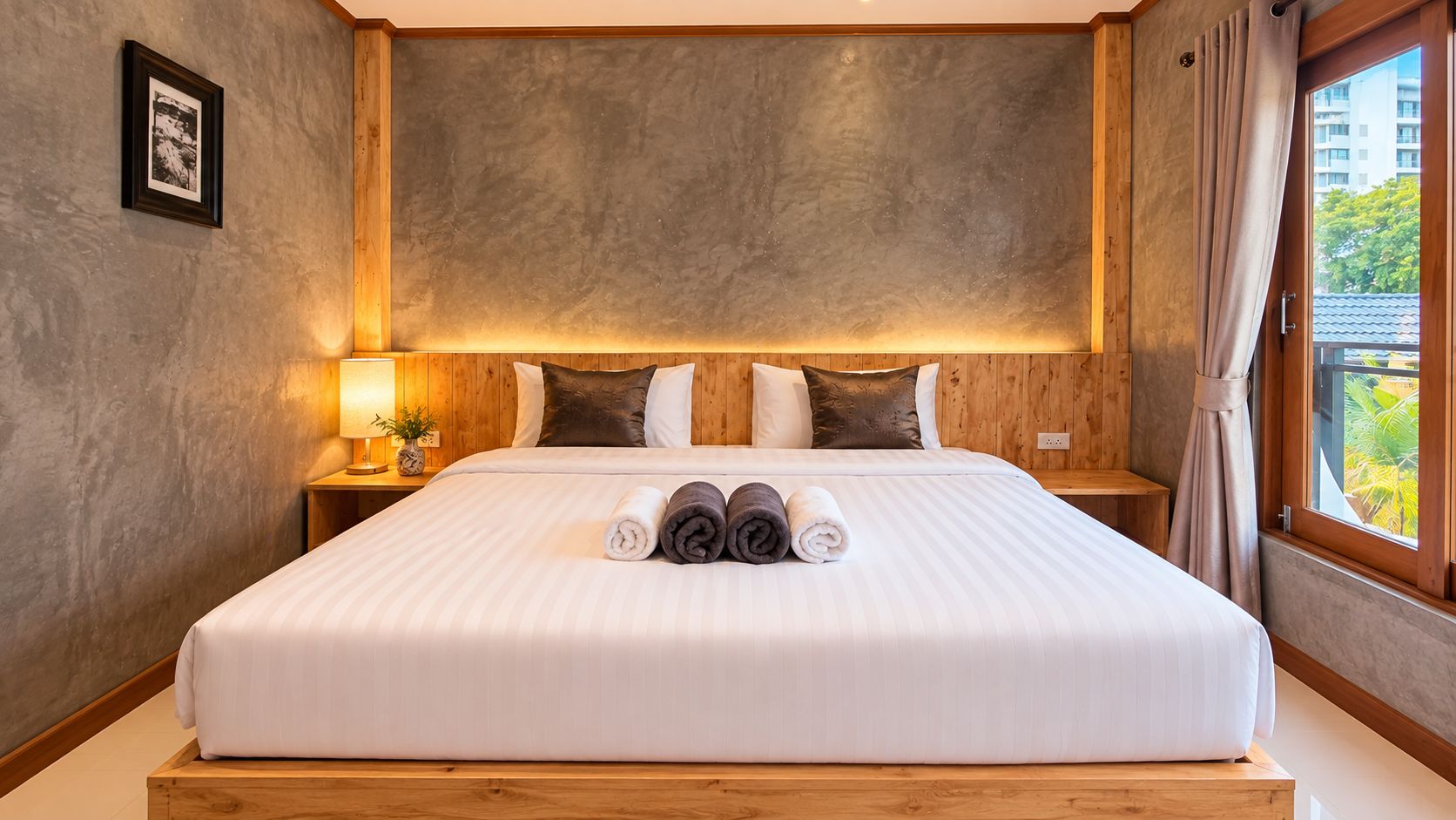 A hotel room with a large bed, wooden headboard, and a view of greenery outside.